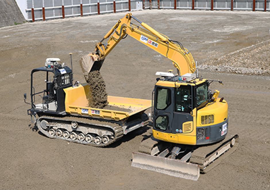 An automated backhoe loads soil and sand into an automated carrier dump truck