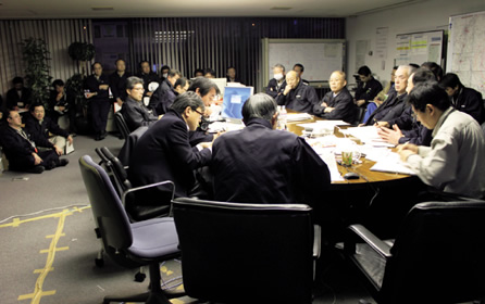 写真：震災対策会議の様子。幹部を囲むように社員が陣取る