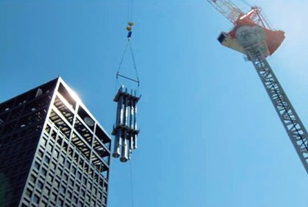 写真：①タワークレーンで，3階分の長さ12mの竪管を一気に揚重する