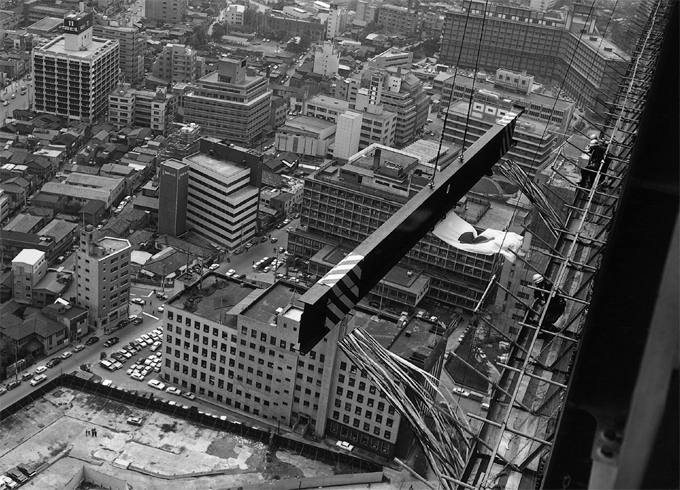 写真：昭和42年4月13日，上棟式が行われ高々と鉄骨の梁が吊り上がる様子