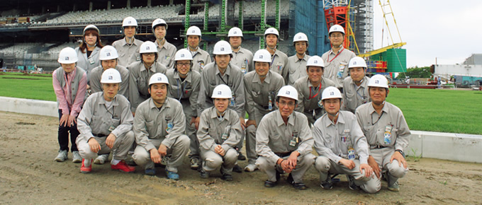 写真：大屋根鉄骨上架作業を前に記念撮影。中段右から三番目が横井所長