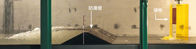 写真：20mの津波を再現した実験（1/100スケール）。津波が防潮堤を超え，建物に迫る