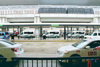 写真：国内線ターミナルの2階を発車するスカイトレインと1階玄関に並ぶシャトルバス