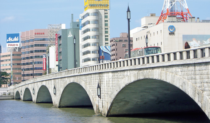 写真：滔々と流れる水に逆らって建つ萬代橋。2004年に国の重要文化財の指定を受けた。市民に愛され続ける名橋である