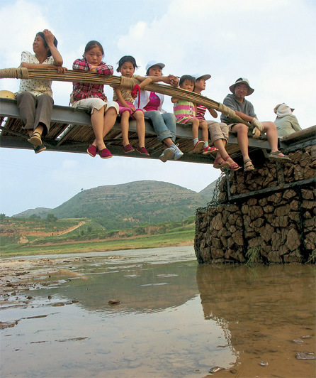 写真：完成した橋に座る住民。男性だけでなく女性や子どもも橋づくりに関わる
