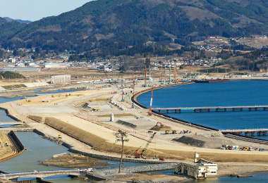 図版：海上輸送で資材を調達するための荷揚げ用仮設桟橋2基（のちに撤去）と海側の第1線提の根固め工がほぼ完成した様子（2015年2月）