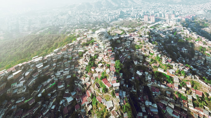 写真：都市周辺の丘の地形に沿って建てられた低層住宅。中央の尾根筋上にロープウェイが通っているのが見える