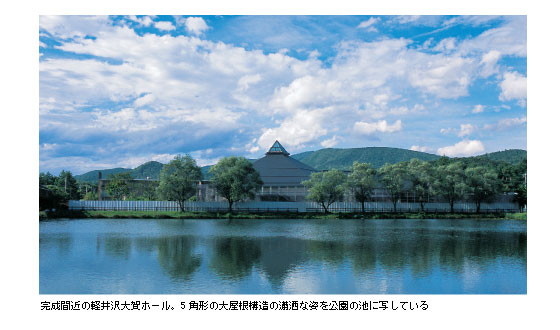 完成間近の軽井沢大賀ホール。5角形の大屋根構造の瀟洒な姿を公園の池に写している