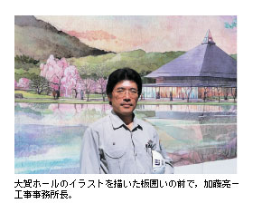 大賀ホールのイラストを描いた板囲いの前で，加藤亮一工事事務所長。