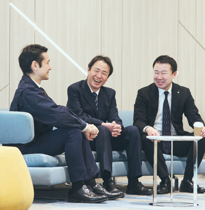 ラウンジスペースのソファーに座り、リラックスした様子で対話する右上肢障がいの男性社員とチームメンバー。本音で語り合える深い絆を象徴する風景の写真