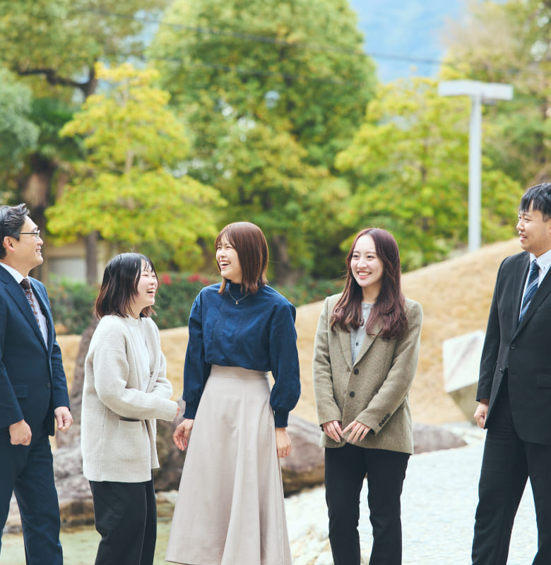 障がいをもつ女性社員を中心に、屋外でチームの仲間5名が横に並び、心から楽しそうに笑い合う集合写真