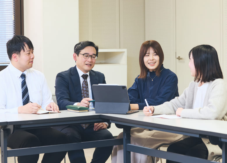 会議室でタブレット端末を囲み、チームメンバーと真剣な表情で意見を交わす女性社員の写真