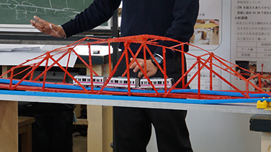 図版：橋の模型に玩具の電車を走らせ実験する班