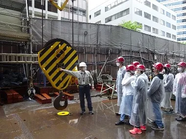 屋上から降ろされたタワークレーンのフックを見る生徒たち