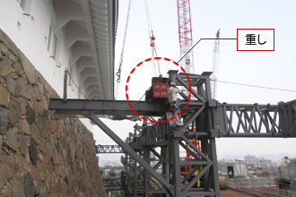 写真：3階南面床のブラケット鉄骨　玉掛・地切　吊りワイヤーが庇に当たらぬよう、根元に重しを載せ安全に吊り重心をずらします。